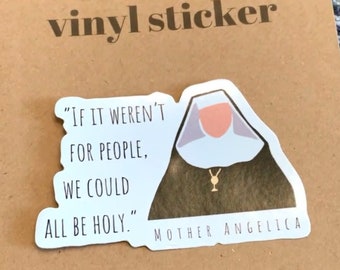 Può includere: Un adesivo in vinile fustellato con un'illustrazione stilizzata di una suora con abito marrone e velo bianco. Il testo recita "If it weren't for people, we could all be holy." e "Mother Angelica" in caratteri neri su sfondo bianco.