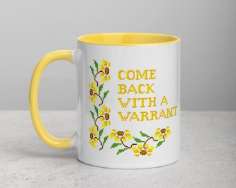 May include: White ceramic mug with a yellow rim. The mug has a floral design and the text "COME BACK WITH A WARRANT" in yellow.