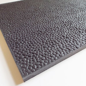 May include: Black rubber floor tile with a textured pebble surface.