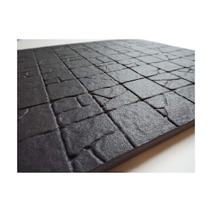 May include: Black foam gaming mat with a textured surface that resembles stone. The mat has a grid pattern.