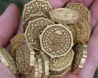 May include: A hand holding a pile of gold-colored metal coins with a skull and crossbones design. The coins have a decorative border and a raised design.