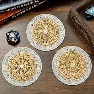 May include: Three round, light-colored coasters with a gold-colored, circular design and an outer ring of letters. A wooden box with dice and a stack of books are also visible. The dice are blue, black, and white.
