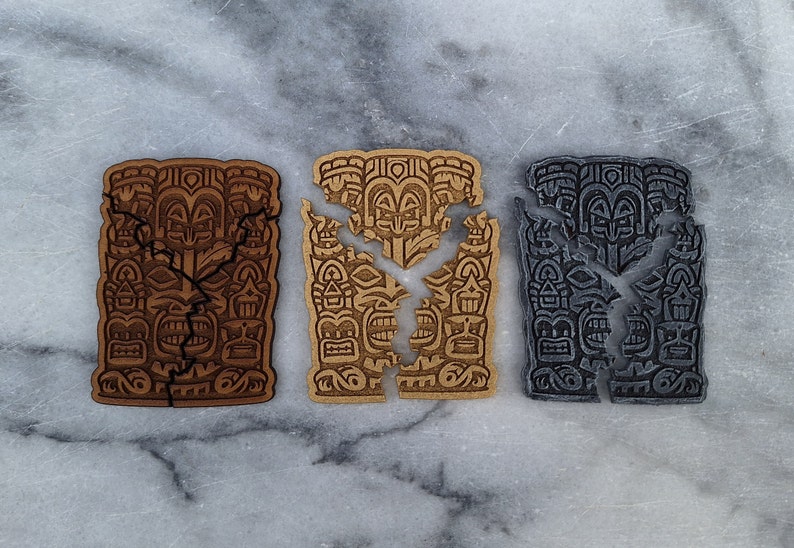 Puede incluir: Tres tallas de madera estilo tiki en tonos marr&oacute;n, beige y gris, cada una con un dise&ntilde;o agrietado. Las tallas presentan caras detalladas y patrones geom&eacute;tricos, sobre un fondo de m&aacute;rmol.