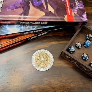 May include: A tabletop gaming scene featuring Dungeons & Dragons books: Dungeon Master's Guide, Monster Manual, and Player's Handbook. A wooden dice tray holds various multi-sided dice. A circular game piece with a cipher design is also present.
