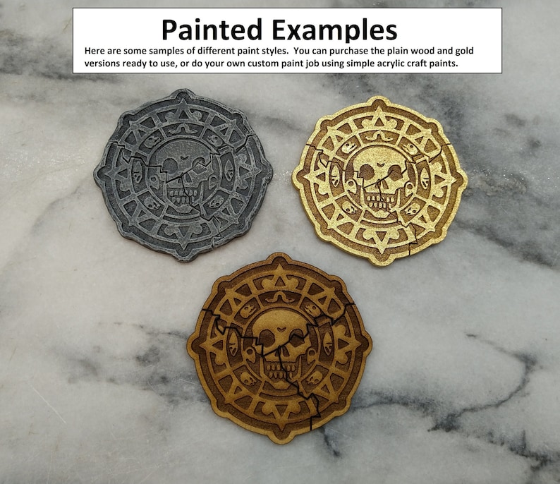 Puede incluir: Tres fichas circulares de madera con un dise&ntilde;o de calavera, cada una pintada de forma diferente. Una es gris, otra dorada y la otra marr&oacute;n c&aacute;lido. El texto "Painted Examples" y otro texto es visible en la parte superior de la imagen.