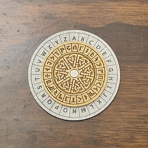 May include: A wooden cipher wheel with a circular design. The outer ring features the alphabet, while the inner circle displays intricate Celtic knot patterns. The wheel is set on a silver-colored base, creating a contrast with the natural wood tones.