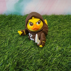May include: A yellow duck wearing a brown hooded cloak and holding a white knife. The duck has a serious expression on its face.