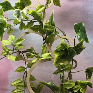 May include: A decorative planter featuring a cat face design, with a wooden trellis structure and artificial ivy. The planter is beige, the trellis is light brown, and the ivy is green with lighter green accents.