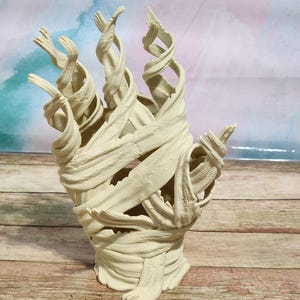 May include: A white, 3D printed sculpture of a hand wrapped in bandages. The sculpture is made of a smooth, white plastic and has a detailed, realistic texture.