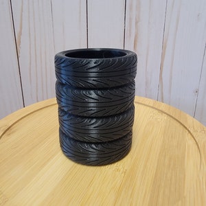 May include: Four black rubber tire-shaped planters stacked on top of each other on a wooden surface.