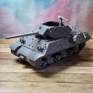 May include: A gray model tank with a long barrel and a rotating turret. The tank has a star emblem on its side and detailed tracks. The model is set against a wooden background.