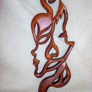 May include: A wooden wall sculpture of two faces intertwined with intricate details. The sculpture is carved from a single piece of wood and features a natural brown finish.