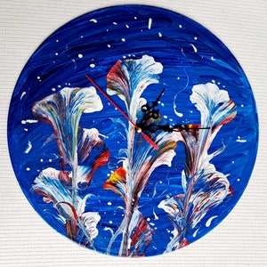Peut inclure: Une horloge circulaire bleue avec un motif floral abstrait blanc, rouge et jaune. Les aiguilles de l'horloge sont noires et rouges.