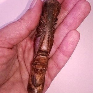 Puede incluir: Una talla de tiki de madera con un acabado marrón y negro. La talla es de una cara con una nariz y una boca grandes.
