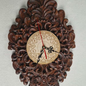 May include: Ornate, dark brown wooden wall clock with a carved floral design. The clock face is light brown with black hands and red second hand. The clock is approximately 12 inches in diameter.