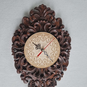 May include: A decorative wooden wall clock with an ornate, dark brown, carved frame. The clock face is light-colored with black numerals and hands, and a red second hand. The clock is approximately 12 inches in height.
