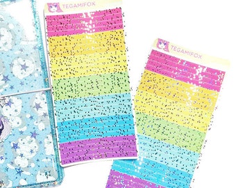 Puede incluir: Una agenda azul claro con un diseño de nubes y estrellas, un cierre de metal plateado y un dije. También hay dos hojas de pegatinas con rayas de purpurina de colores arcoíris y el texto "TEGAMIFOX". Los artículos están sobre un fondo blanco.