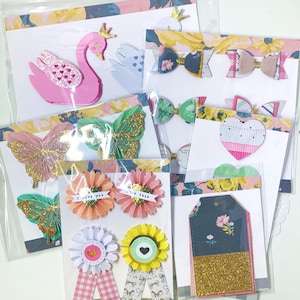 Peut inclure: Divers embellissements en papier faits à la main, dont un cygne rose couronné, des papillons, des nœuds, des fleurs, des cœurs et des étiquettes. Les embellissements présentent des paillettes, du papier à motifs et du ruban, parfaits pour le scrapbooking.