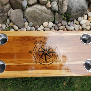 Puede incluir: Bandeja rectangular de madera con cuatro portavasos de acero inoxidable. La bandeja tiene un diseño de rosa de los vientos en el centro. La madera tiene un tono marrón cálido natural. Mide unos 76 cm.