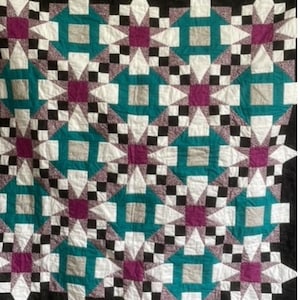 May include: A quilt with a geometric pattern of black, white, teal and purple stars. The quilt is made of fabric squares sewn together to create a repeating pattern.