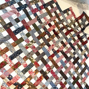 May include: A white quilt with a patchwork design. The quilt is made up of squares of different fabrics, each with a unique pattern. The quilt is pinned together with safety pins.