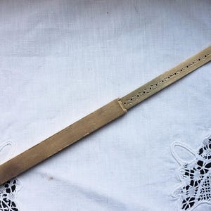 以下が含まれることがあります： エッチングされたマーキングと装飾的な切り抜きが施された、ヴィンテージの真鍮製定規。定規は長方形で、金色の金属でできているようです。レースのディテールが施された、白くテクスチャ加工された表面に置かれています。