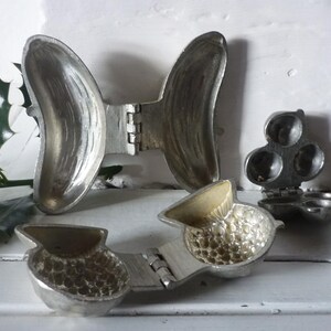 May include: Three antique, hinged, cast-metal molds. One is butterfly-shaped, another is a three-sectioned sphere, and the third is a pear-shaped mold. All are open, revealing their interior shapes and textures.