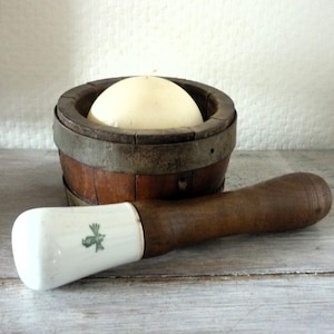 Puede incluir: Un mortero y un pilón de madera con un pilón de porcelana blanca. El mortero está hecho de madera y tiene una banda de metal alrededor de la parte superior. El pilón tiene un diseño floral verde en el lateral.