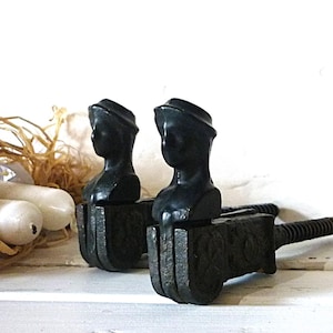 May include: Two black antique bookends, each featuring a bust of a woman with a headscarf. The bookends have a dark, textured finish and a screw mechanism. The background is white.