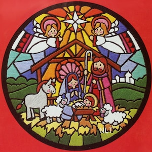 May include: A circular embroidered patch featuring a nativity scene with a stained glass aesthetic. It depicts a central manger with a baby, two figures, a donkey, and two sheep under a star, framed by two angels and the letters NLT in white.