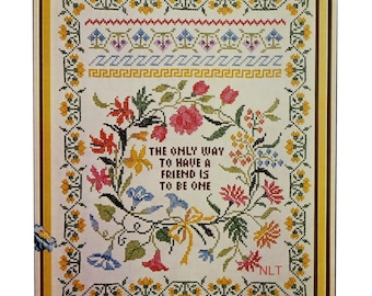 May include: A framed cross-stitch sampler featuring a floral wreath surrounding the text THE ONLY WAY TO HAVE A FRIEND IS TO BE ONE. The design includes a yellow floral border, geometric patterns, and red, blue, and green flowers.