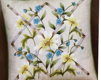 May include: A square pillow featuring crewelwork embroidery of white daisies and small blue flowers intertwined with a brown lattice pattern on a natural linen fabric. The pillow has a green border and the letters NLT printed in the bottom right corner.