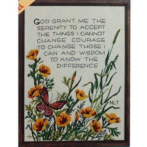 May include: Embroidered artwork in a dark wood frame. The artwork features the text "God grant me the serenity..." with a floral and butterfly design in shades of yellow, green, and red. The artwork is signed "NLT".