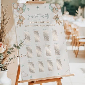 May include: A baptism seating chart on an easel. The sign features a teddy bear holding balloons, with the text "your seat awaits" and "Oliver's Baptism". The date and location are also displayed. The design includes stars and clouds.