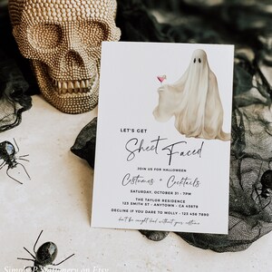 Może przedstawiać: Karta zaproszenia na Halloween z napisem "LET'S GET Sheet Faced". Karta zawiera akwarelową ilustrację ducha trzymającego koktajl. Widoczne są również dekoracyjne pająki i złota czaszka.
