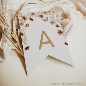 May include: A white pennant banner with a gold letter A and a floral border. The flowers are in shades of red, orange, and yellow. There is a butterfly in the top right corner.