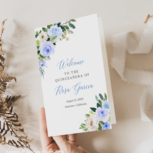 May include: A white card with blue flowers in the corners. The text reads "Welcome to the Quinceañera of Rosa Garcia August 25, 20XX Anytown, California"