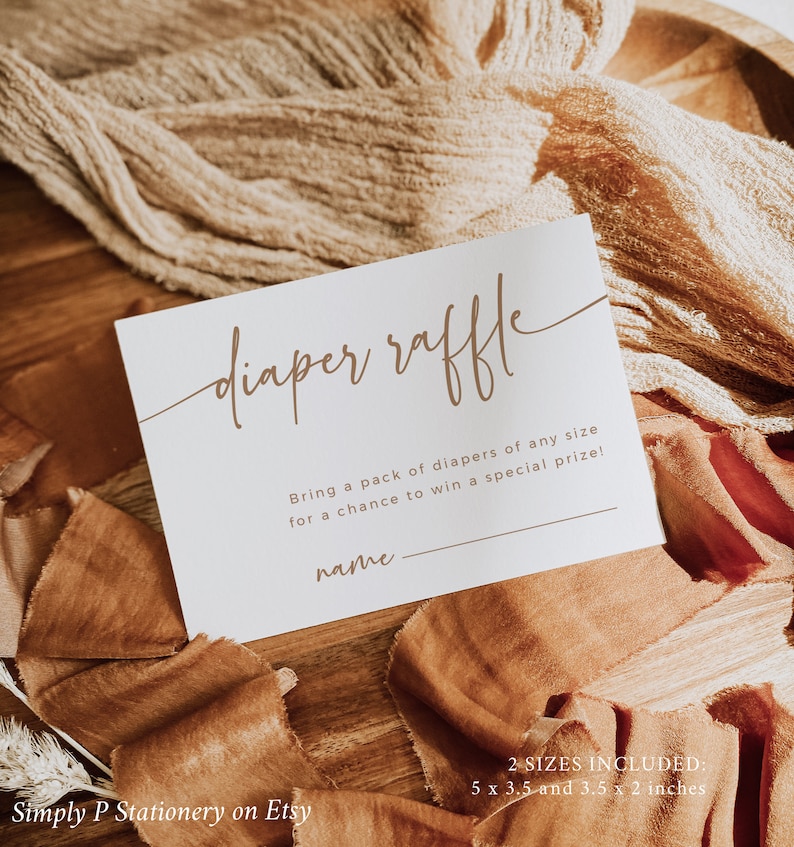 May include: A white card with brown text that says "diaper raffle". The card has a line for a name and the text "Bring a pack of diapers of any size for a chance to win a special prize!"  The card is on a wooden surface with brown fabric.