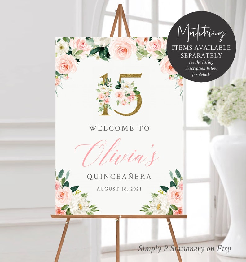 May include: A white welcome sign with pink and white flowers and greenery. The sign has gold glitter lettering that says "15" and "Welcome to Olivia's Quincea&ntilde;era August 16, 2021".