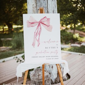 May include: A white welcome sign with a pink watercolor bow and the text "welcome to Blythe's graduation party Cedar Valley High School Class of 20XX".