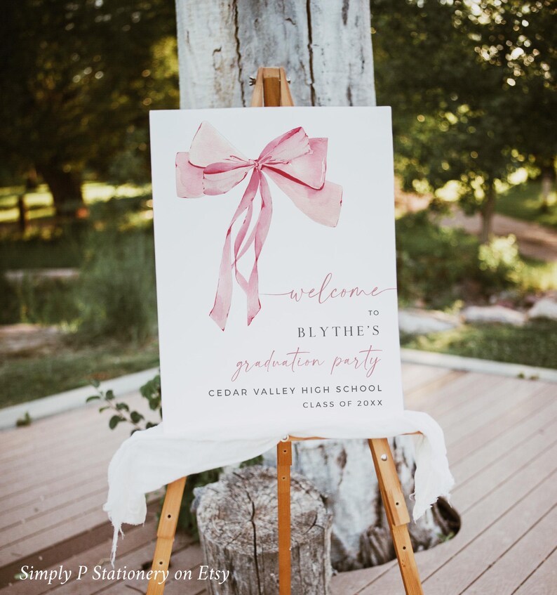 May include: A white welcome sign with a pink watercolor bow and the text "welcome to Blythe's graduation party Cedar Valley High School Class of 20XX".