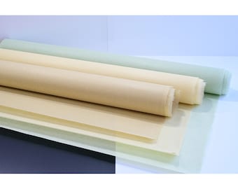 May include: Three rolls of paper in different shades of beige and green. The paper is rolled up and the ends are visible. The paper is on a white surface.