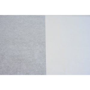 May include: A close-up of two pieces of fabric. The fabric on the left is a light gray, textured material. The fabric on the right is a smooth, white material.