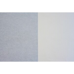 May include: A close-up of two pieces of paper, one is a light gray and the other is a white.