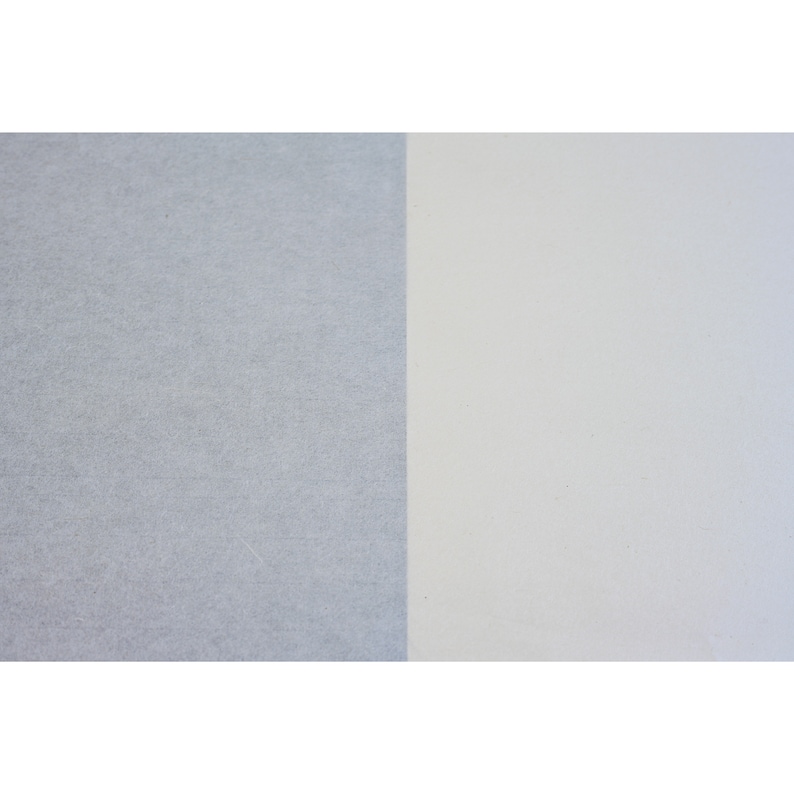 May include: A close-up of two pieces of paper, one is a light gray and the other is a white.