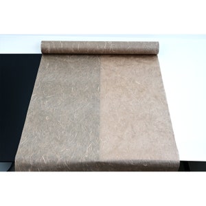 K&ouml;nnte beinhalten: Eine Rolle braunes, strukturiertes Papier mit einem dunkleren braunen Abschnitt auf der linken Seite. Das Papier ist abgewickelt und liegt flach auf einer wei&szlig;en Oberfl&auml;che.