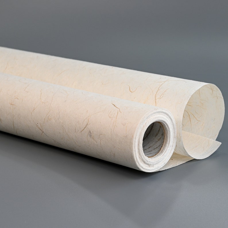 Pu&ograve; includere: Un rotolo di carta testurizzata color avorio con un aspetto di fibra naturale. La carta &egrave; arrotolata e l'estremit&agrave; &egrave; visibile.