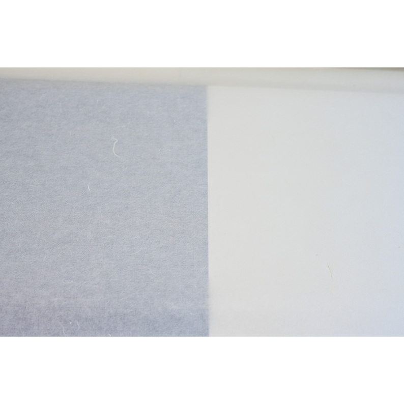 May include: A close-up of two different types of paper. The left side of the image shows a light gray textured paper. The right side of the image shows a white smooth paper.