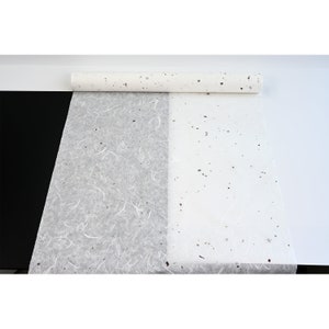 K&ouml;nnte beinhalten: Eine Rolle wei&szlig;es, strukturiertes Papier mit einem gesprenkelten Muster. Das Papier ist teilweise abgewickelt und zeigt eine strukturierte Seite und eine gesprenkelte Seite.