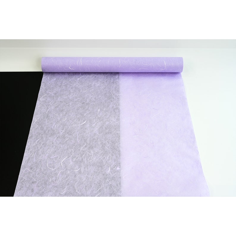 K&ouml;nnte beinhalten: Eine Rolle helllila Seidenpapier mit einer strukturierten, zerknitterten Oberfl&auml;che. Das Papier ist teilweise abgewickelt und zeigt eine wei&szlig;e Seite.